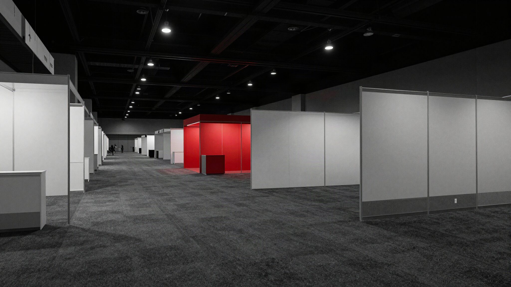 Empty convention hall after hours with rows of trade show booths and one booth lit red