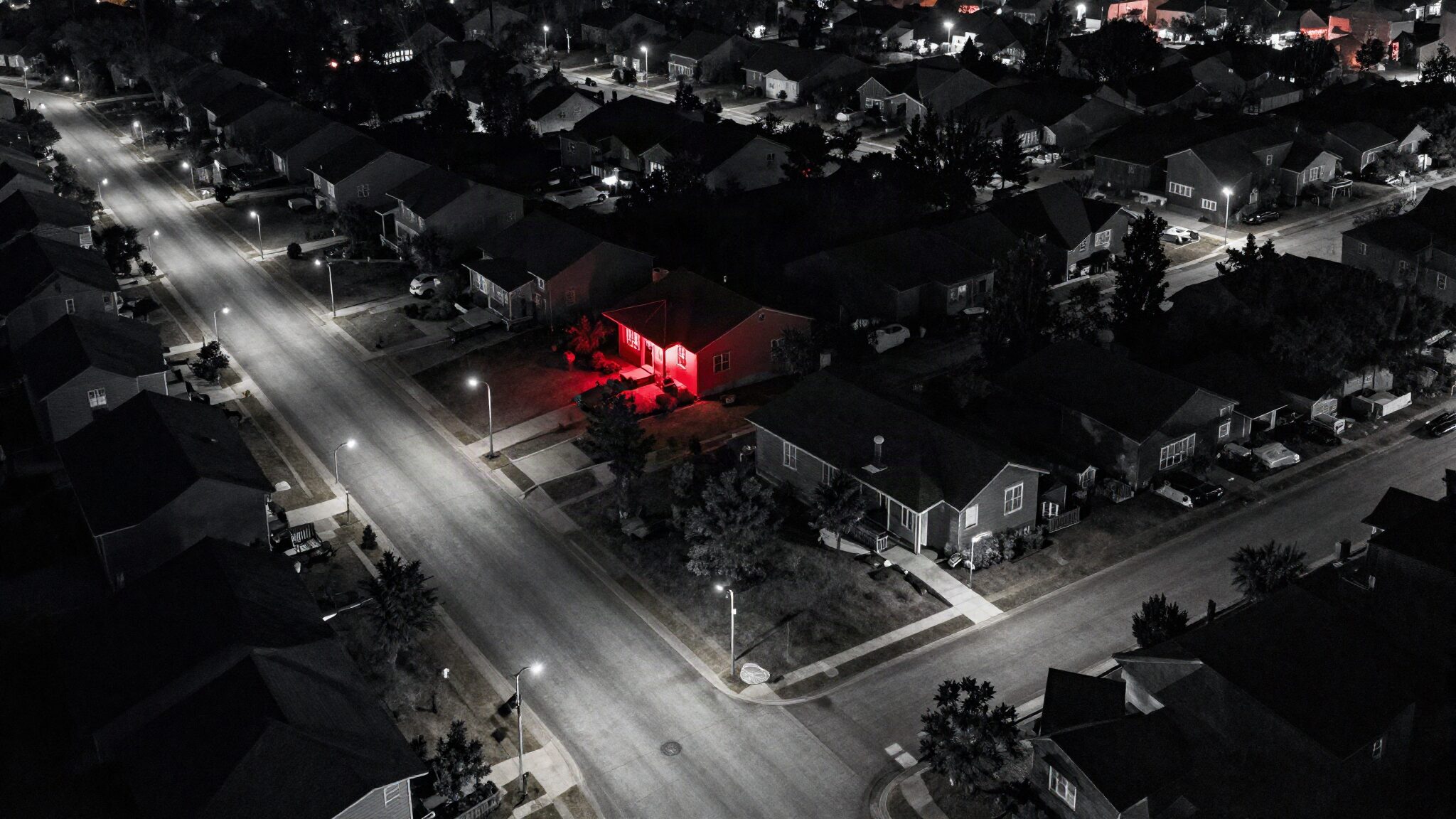 Aerial night view of a suburban neighbourhood street grid with a single house porch lit in red